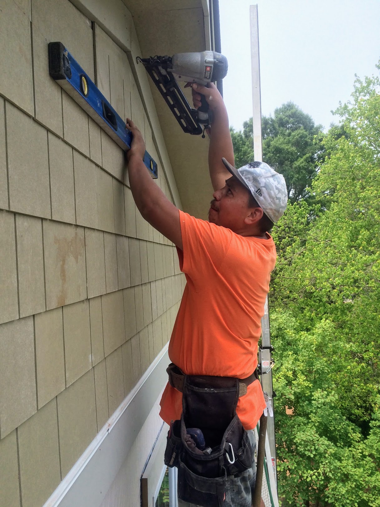 Crew member installing fiber cement shingle siding with a level and nail gun